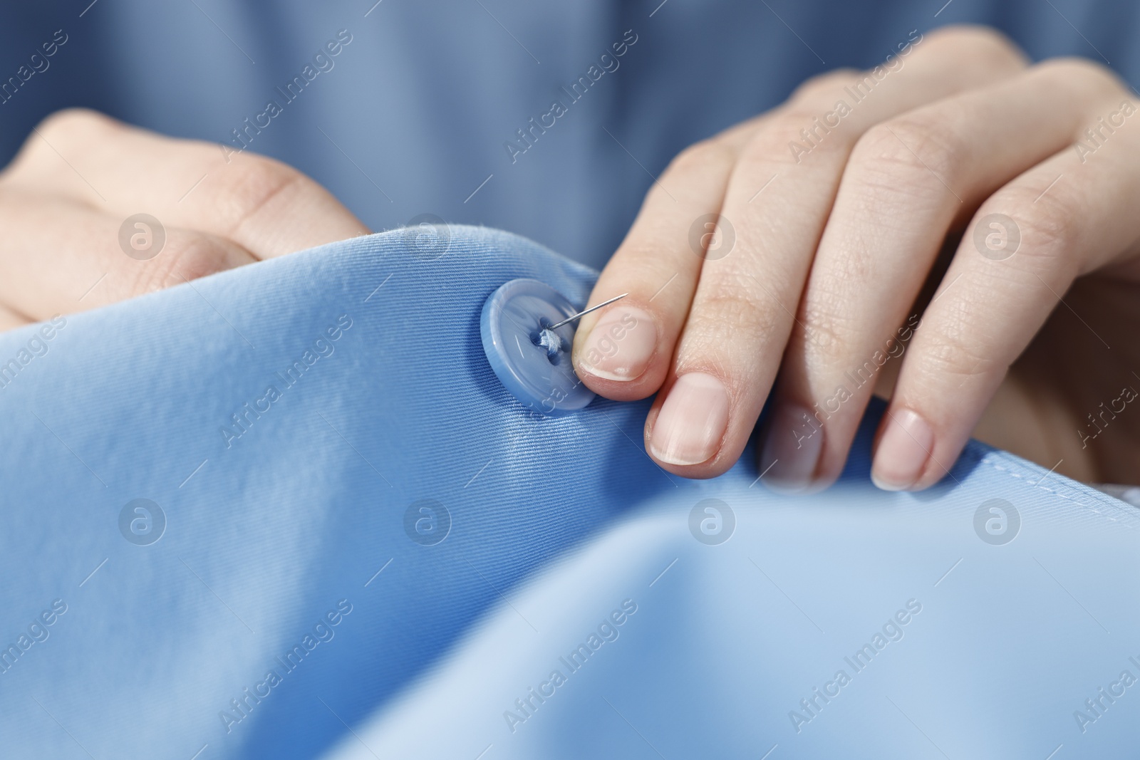 Photo of Woman sewing button with needle and thread onto blue shirt, closeup