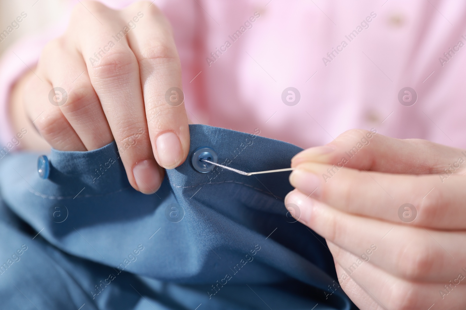 Photo of Woman sewing button with needle and thread onto blue shirt, closeup