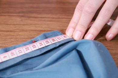 Photo of Woman with measuring tape and blue shirt working at wooden table, closeup