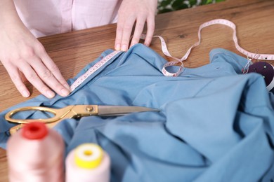 Photo of Woman with measuring tape and blue shirt working at wooden table, closeup