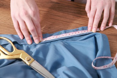 Photo of Woman with measuring tape and blue shirt working at wooden table, closeup