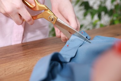 Photo of Woman cutting blue fabric at wooden table in workshop, closeup