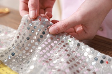 Photo of Woman sewing fabric with sequins at table, closeup