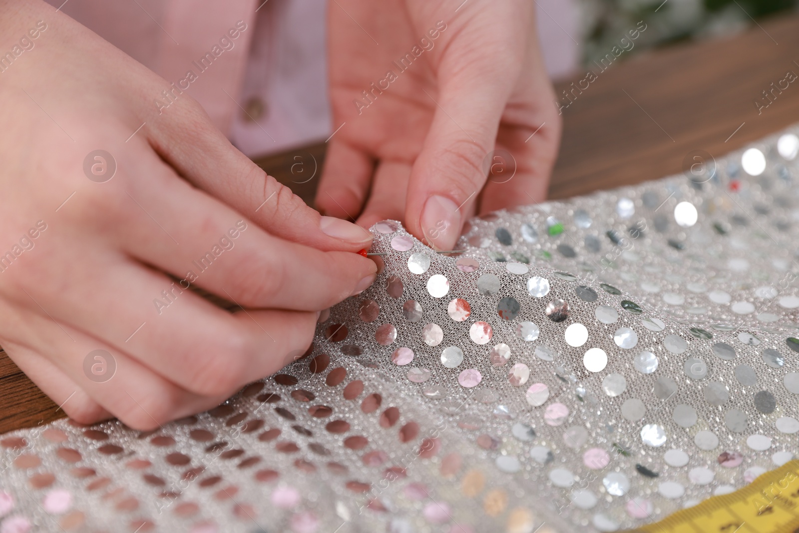 Photo of Woman sewing fabric with sequins at table, closeup