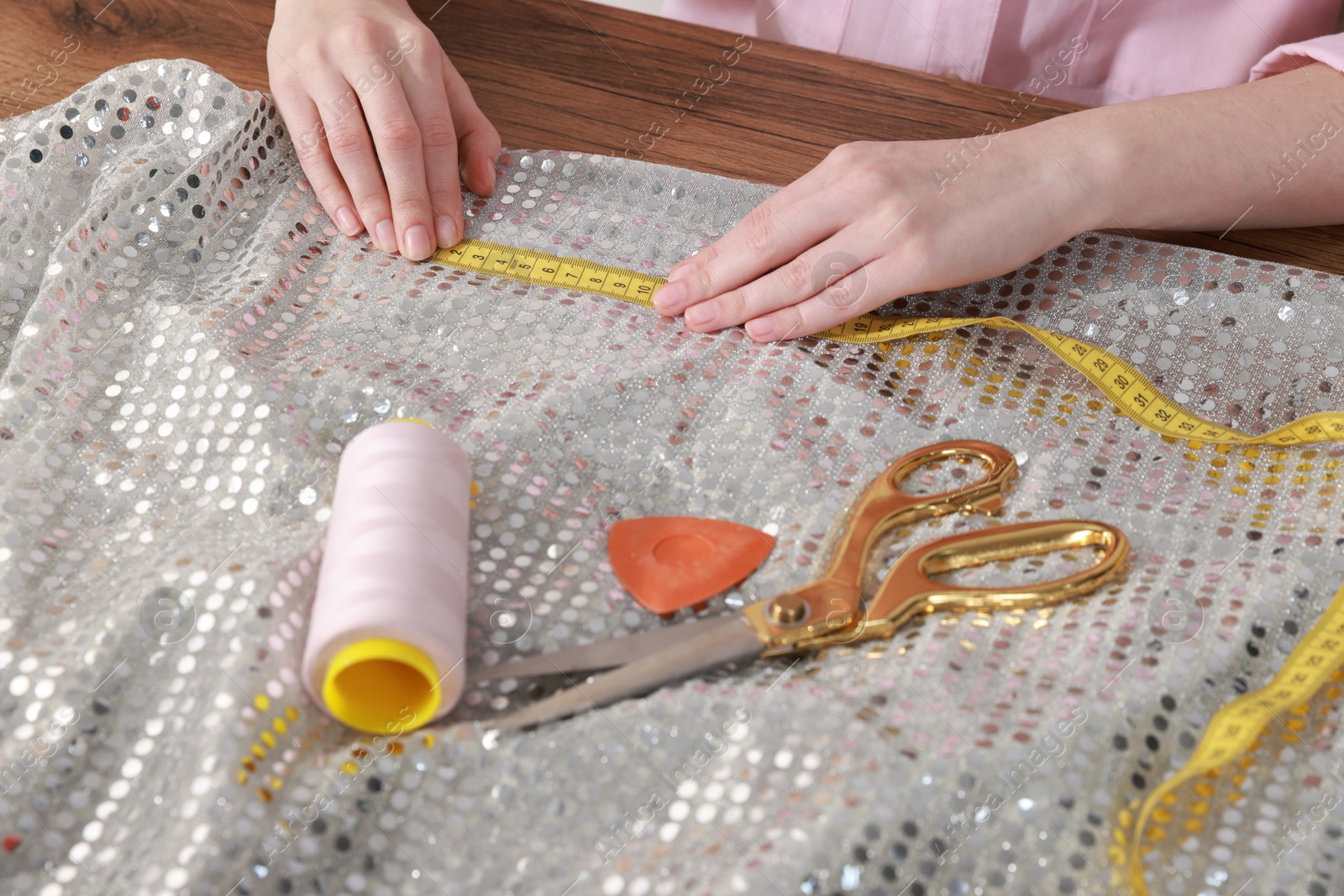 Photo of Woman with measuring tape and shiny fabric working at wooden table, closeup