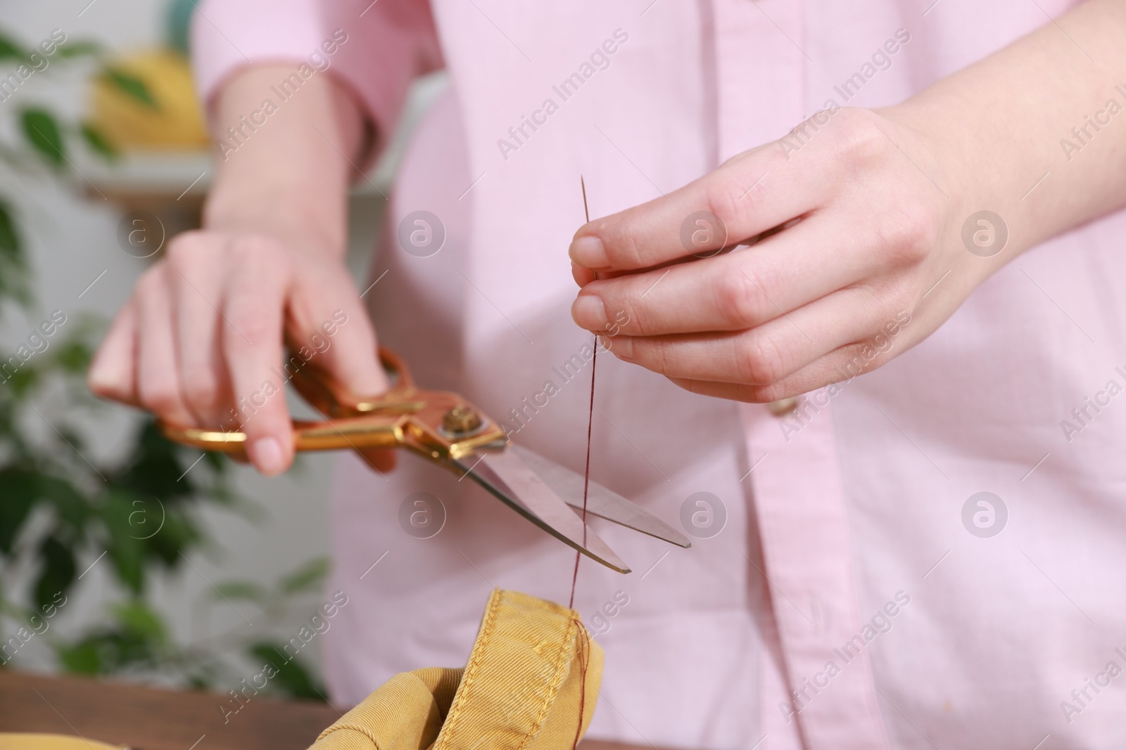 Photo of Woman sewing shirt with needle and thread indoors, closeup