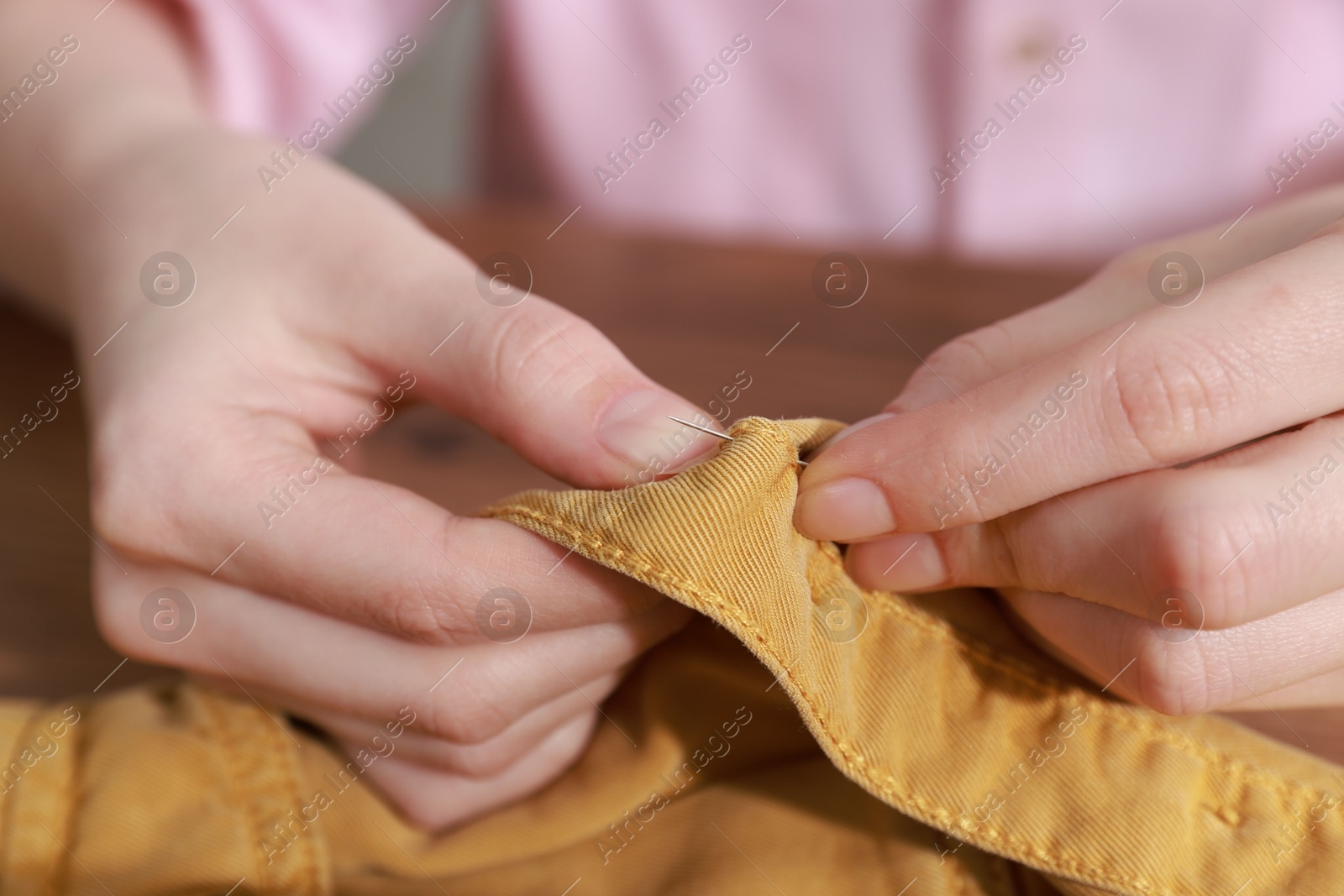 Photo of Woman sewing shirt with needle at table indoors, closeup