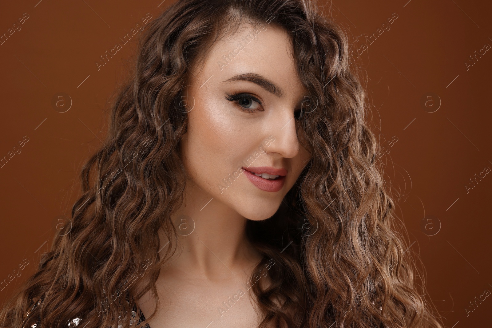 Photo of Beautiful young woman with long curly hair on brown background, closeup