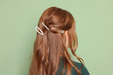 Photo of Teenage girl with stylish hair clips on light green background, back view