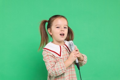 Photo of Cute girl with microphone singing on green background