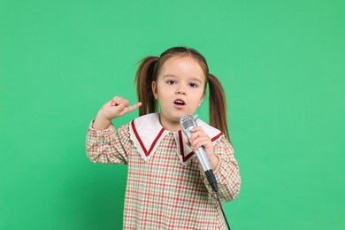 Photo of Cute girl with microphone singing on green background