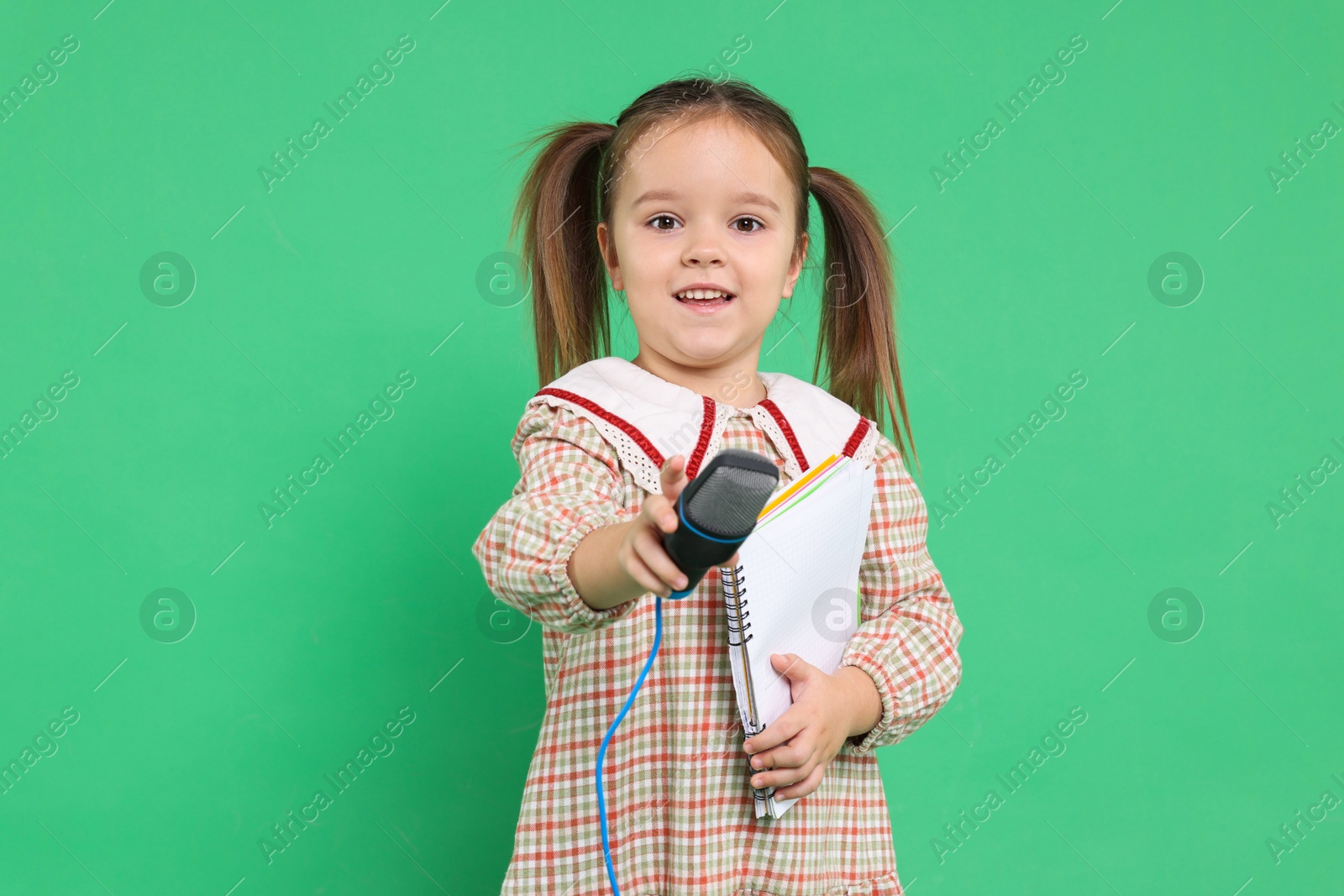 Photo of Smiling girl with microphone and notebook on green background