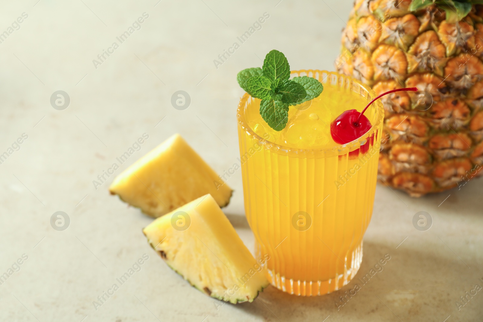 Photo of Tasty pineapple cocktail with mint and cherry in glass served on light table