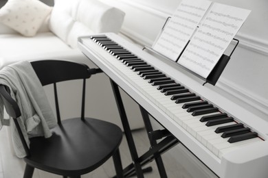 Photo of Synthesizer with music sheets and chair at home, closeup