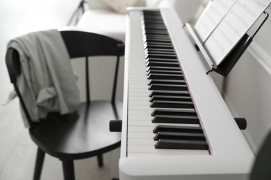 Photo of Synthesizer with music sheets and chair at home, closeup