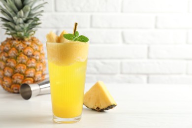 Photo of Tasty pineapple cocktail with mint in glass on light table against white brick wall, space for text