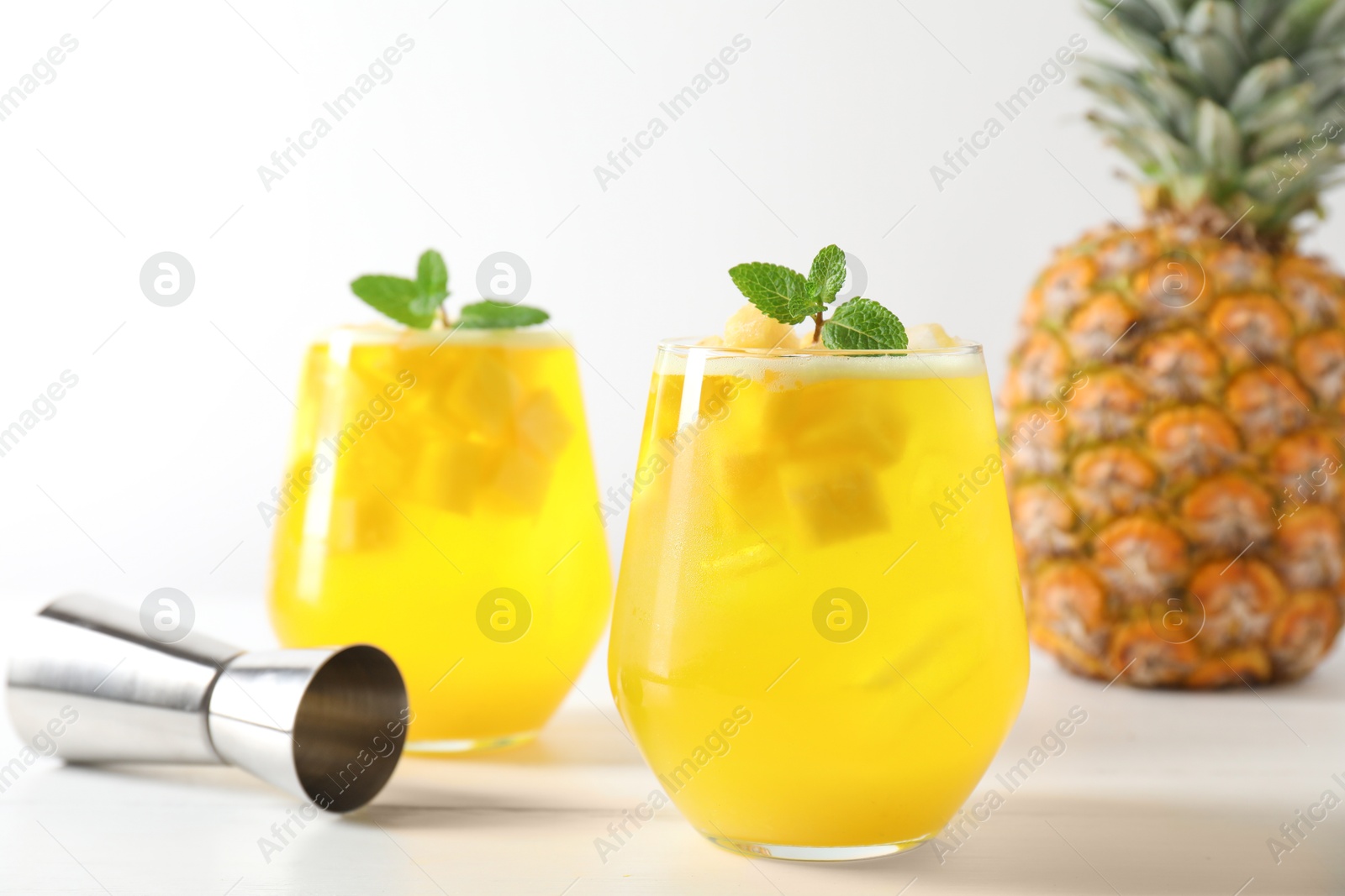 Photo of Tasty pineapple cocktail with mint in glasses and jigger on light table, closeup