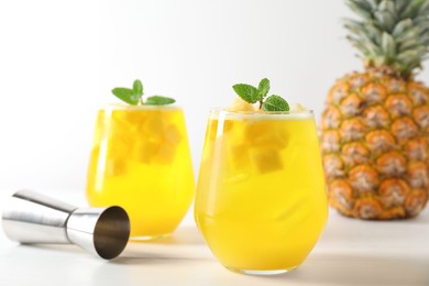 Photo of Tasty pineapple cocktail with mint in glasses and jigger on light table, closeup