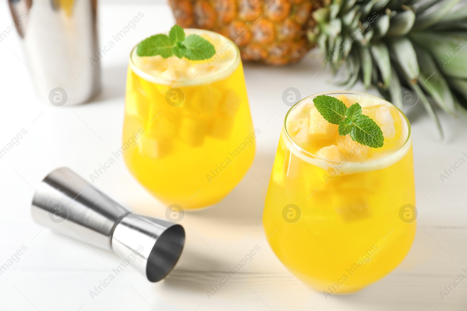 Photo of Tasty pineapple cocktail with mint in glasses and jigger on light table, closeup