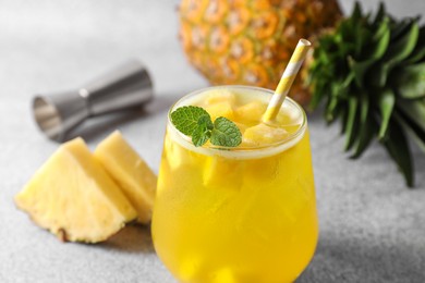 Photo of Tasty pineapple cocktail with mint in glass on gray table, closeup