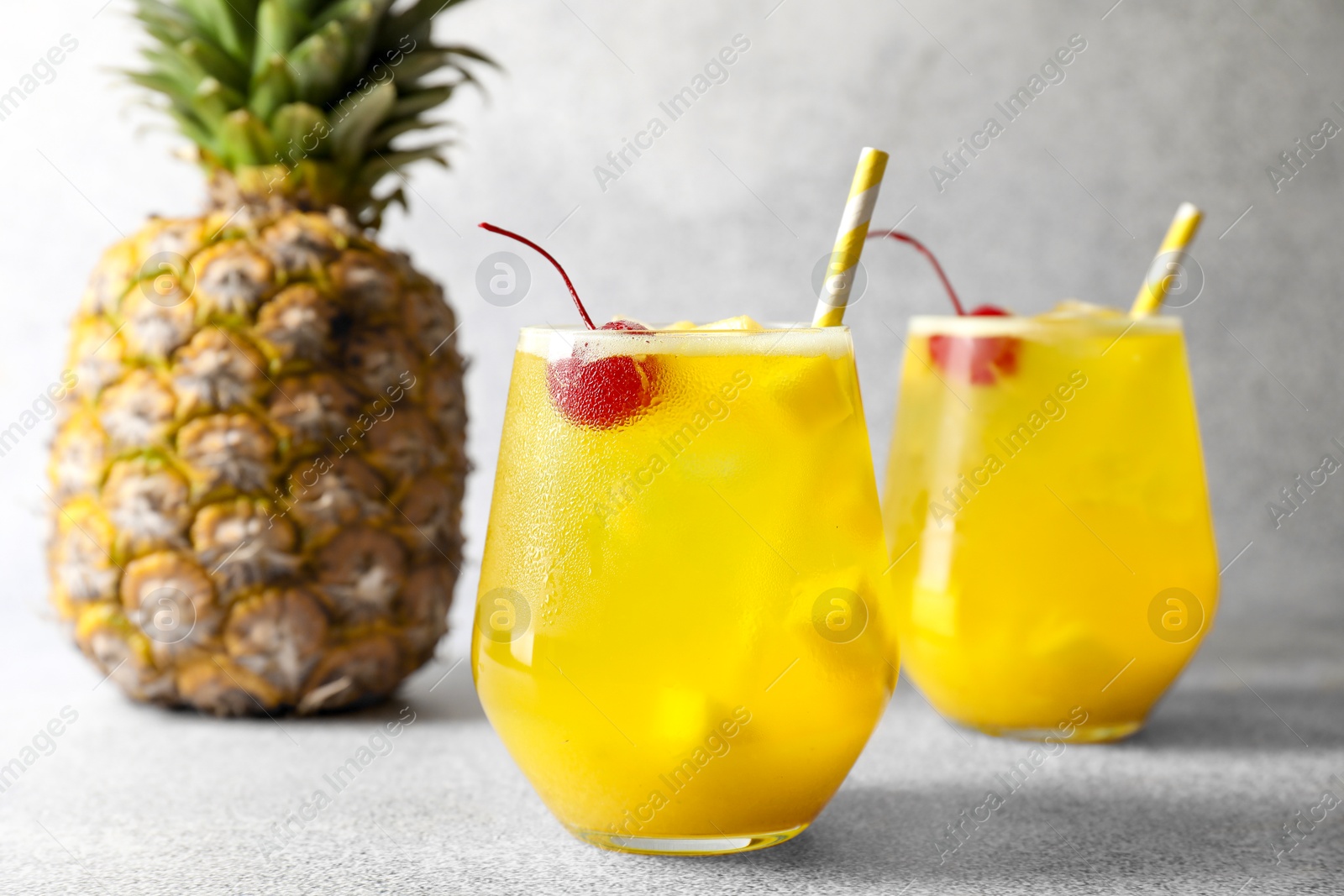 Photo of Tasty pineapple cocktail with cherry in glasses on gray table, closeup