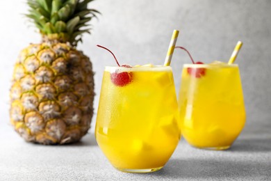 Photo of Tasty pineapple cocktail with cherry in glasses on gray table, closeup