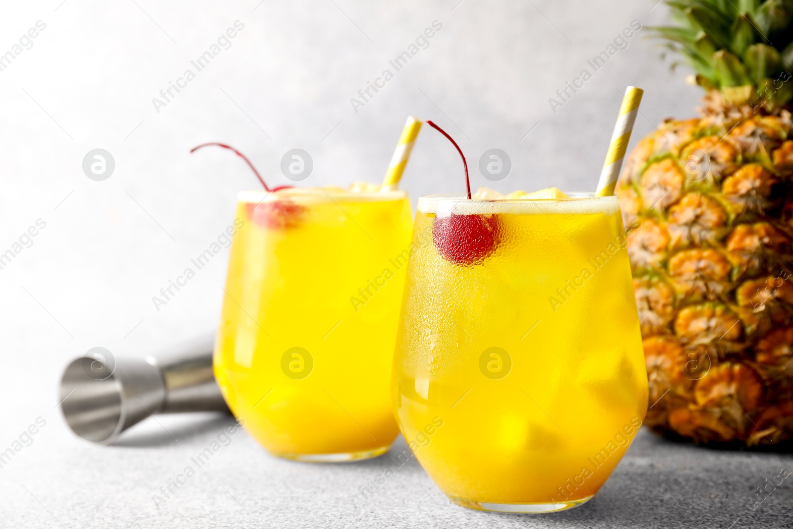 Photo of Tasty pineapple cocktail with cherry in glasses on gray table, closeup