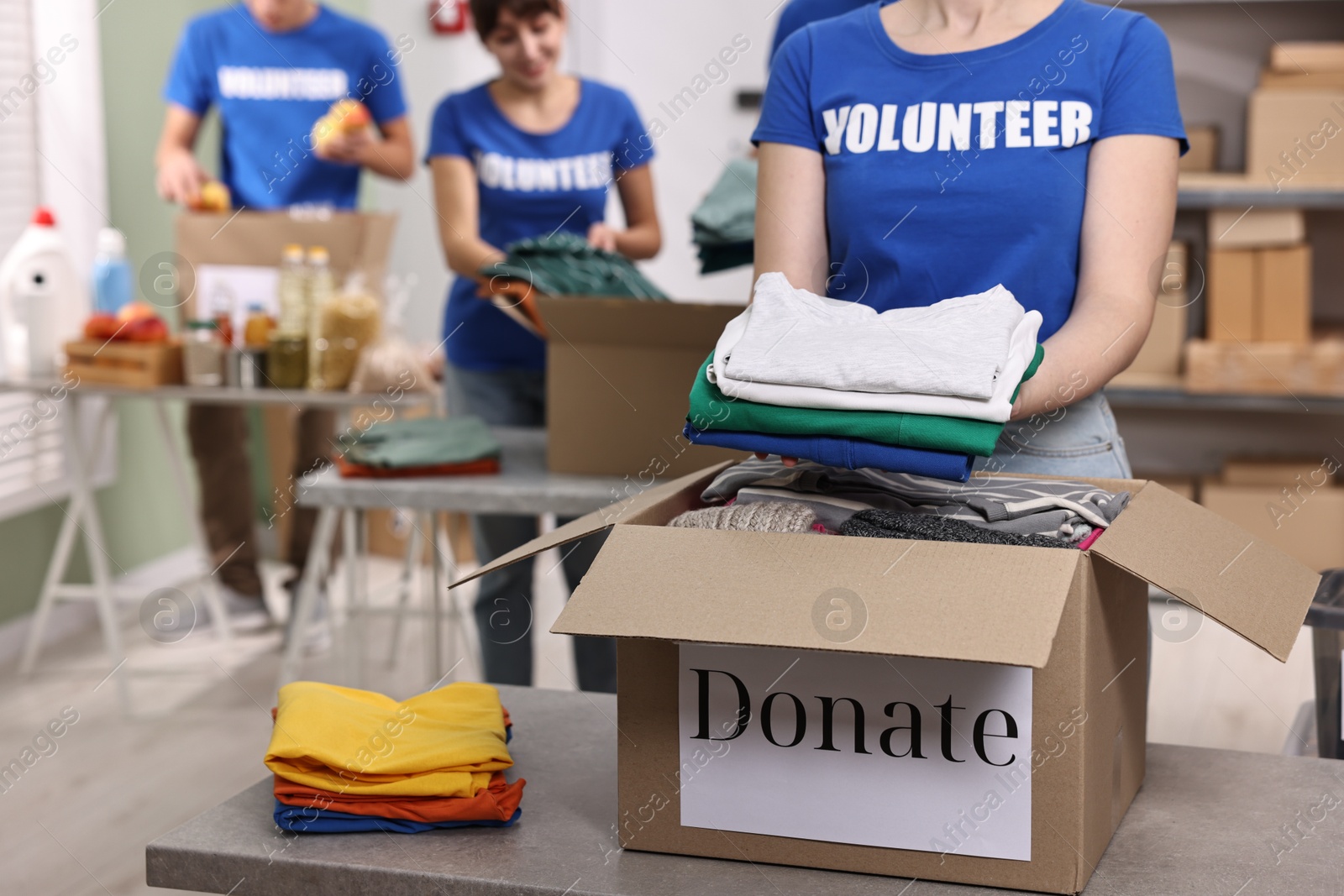 Photo of Group of volunteers packing donation goods at tables indoors, selective focus