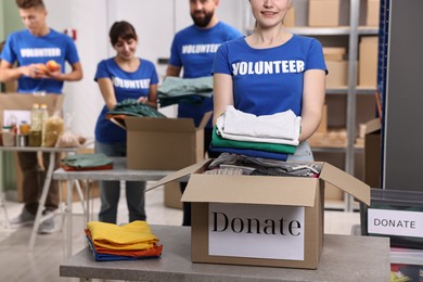 Photo of Group of volunteers packing donation goods at tables indoors, selective focus