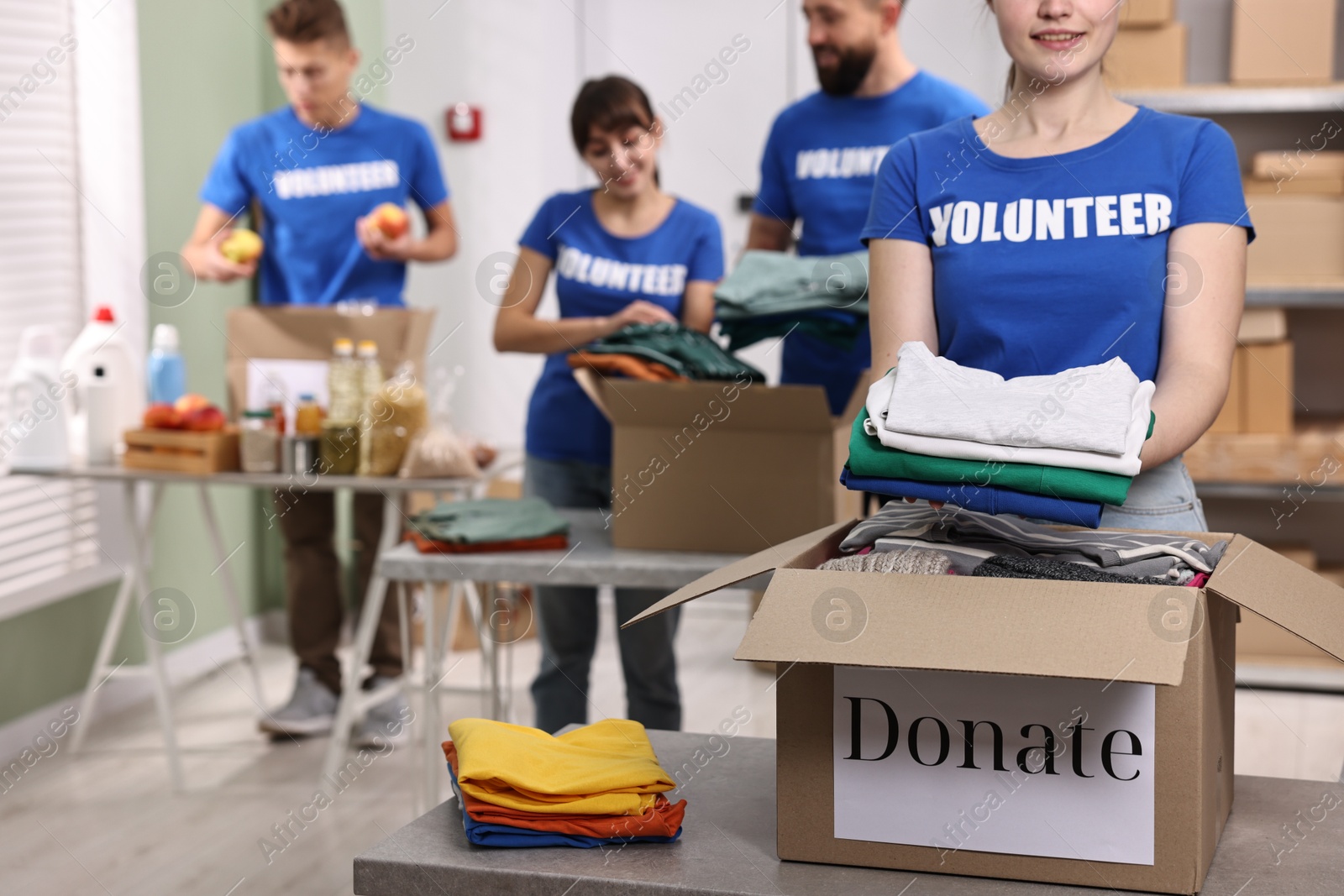 Photo of Group of volunteers packing donation goods at tables indoors, selective focus