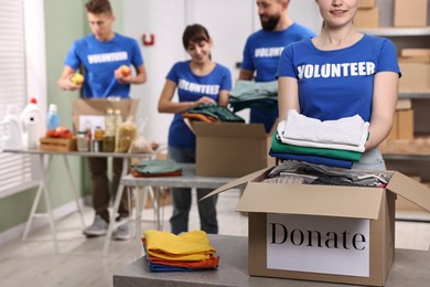 Photo of Group of volunteers packing donation goods at tables indoors, selective focus