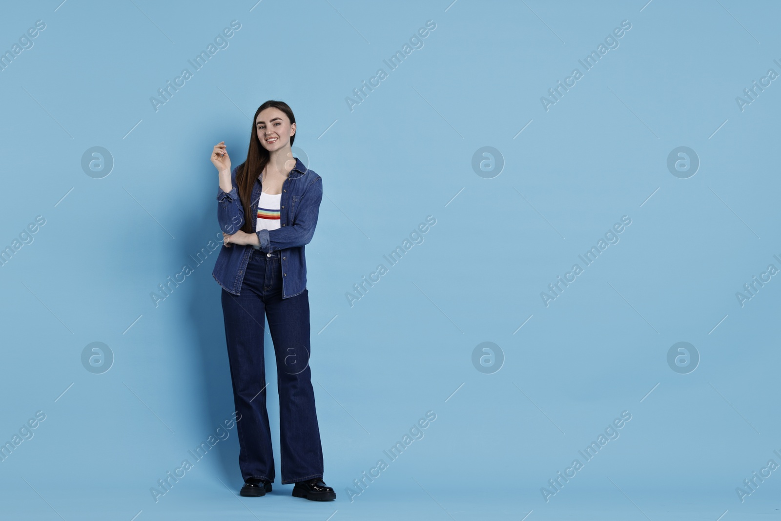 Photo of Smiling woman in stylish jeans on light blue background. Space for text