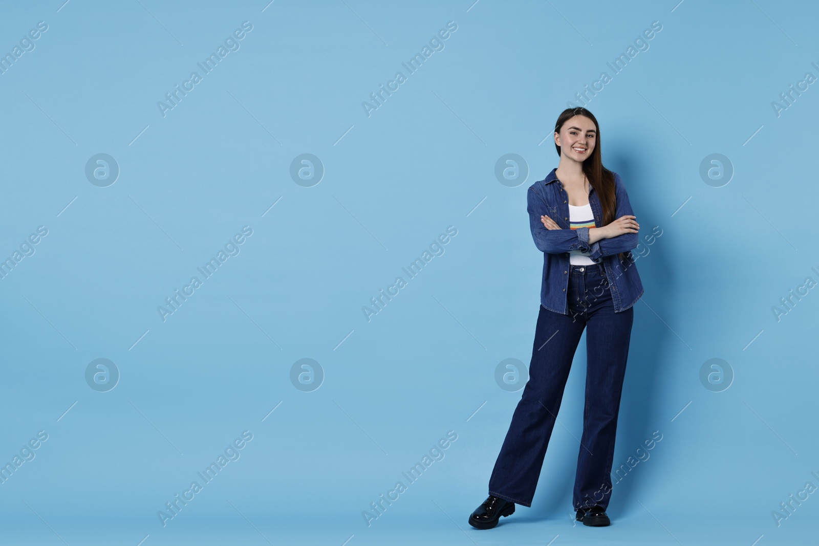 Photo of Smiling woman in stylish jeans on light blue background. Space for text