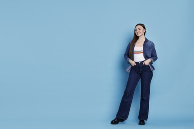 Photo of Smiling woman in stylish jeans on light blue background. Space for text