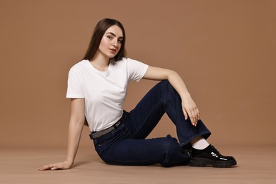 Photo of Beautiful young woman in stylish jeans on brown background