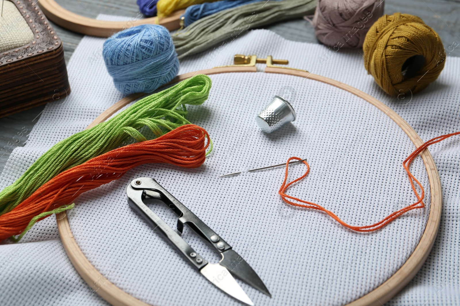 Photo of Different sewing supplies for embroidery on grey wooden table, closeup