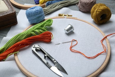 Photo of Different sewing supplies for embroidery on grey wooden table, closeup