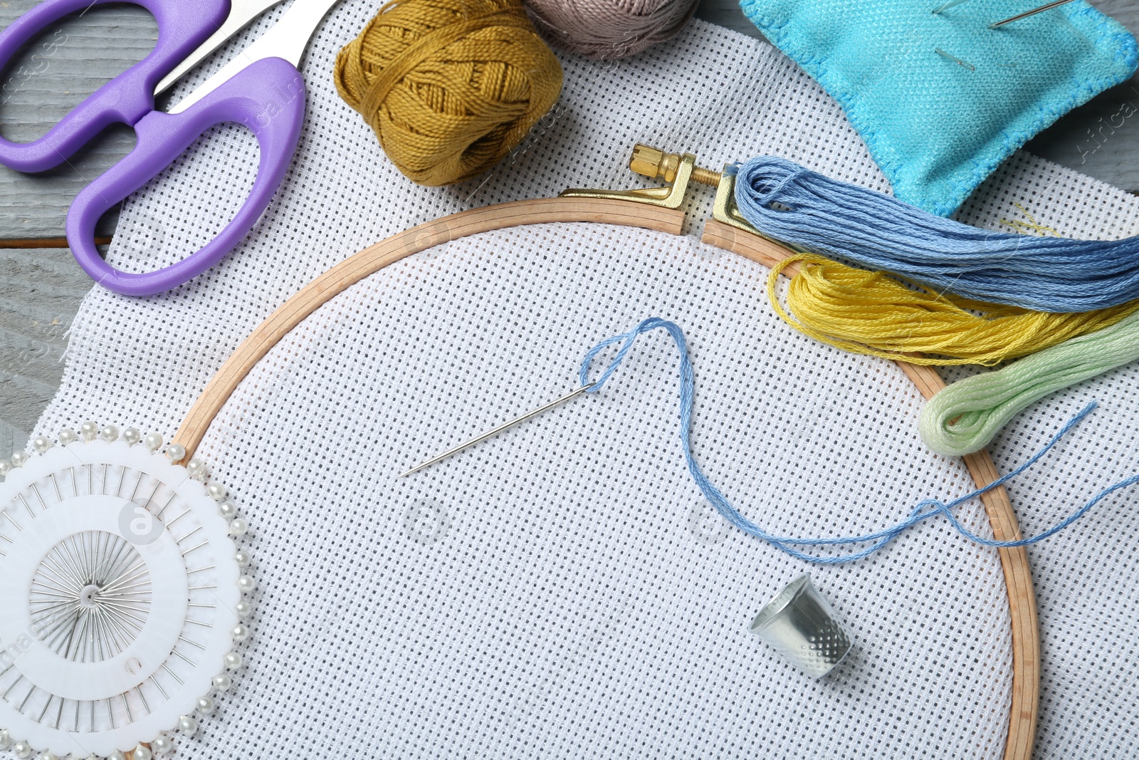 Photo of Different sewing supplies for embroidery on grey wooden table, flat lay