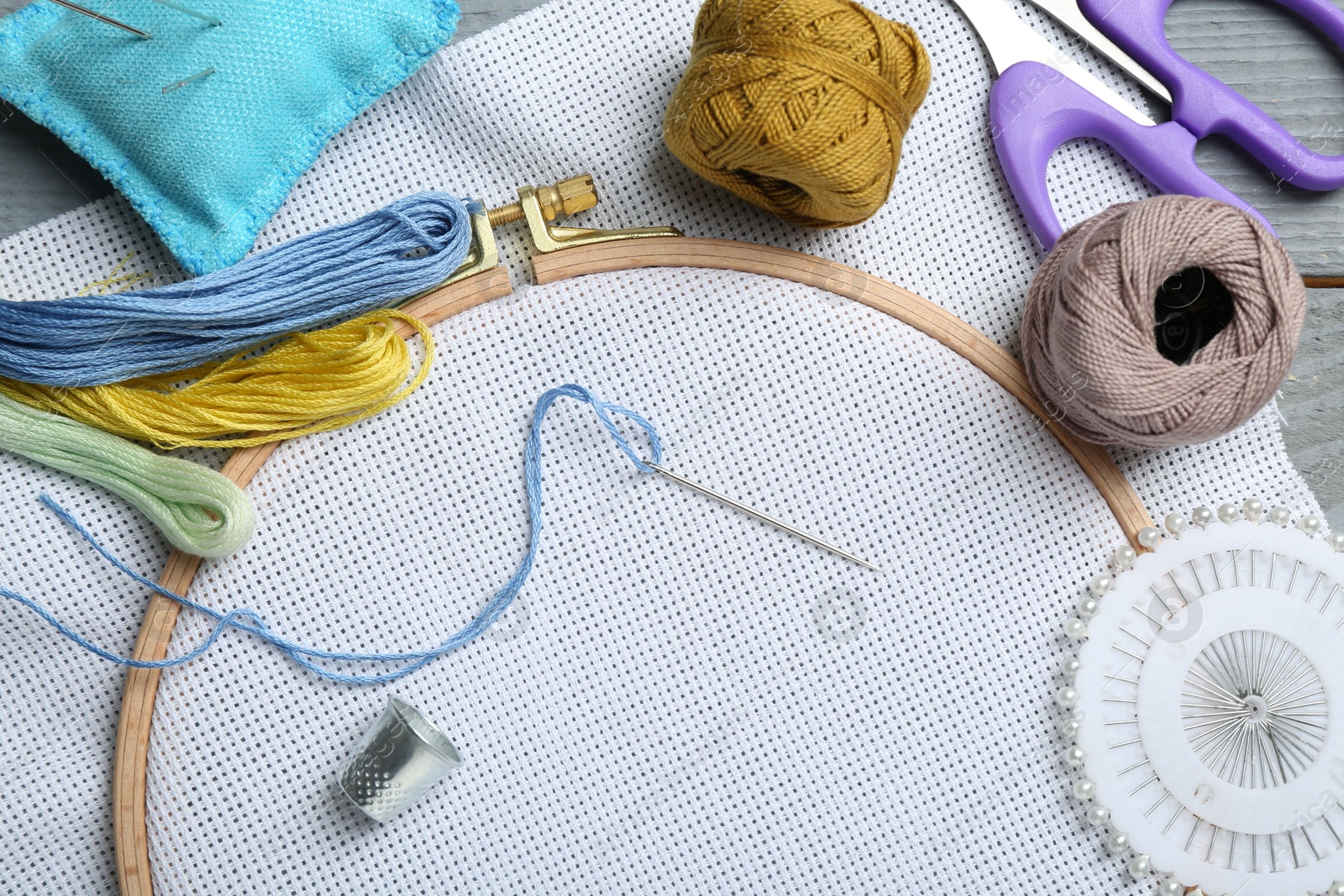 Photo of Different sewing supplies for embroidery on grey wooden table, flat lay