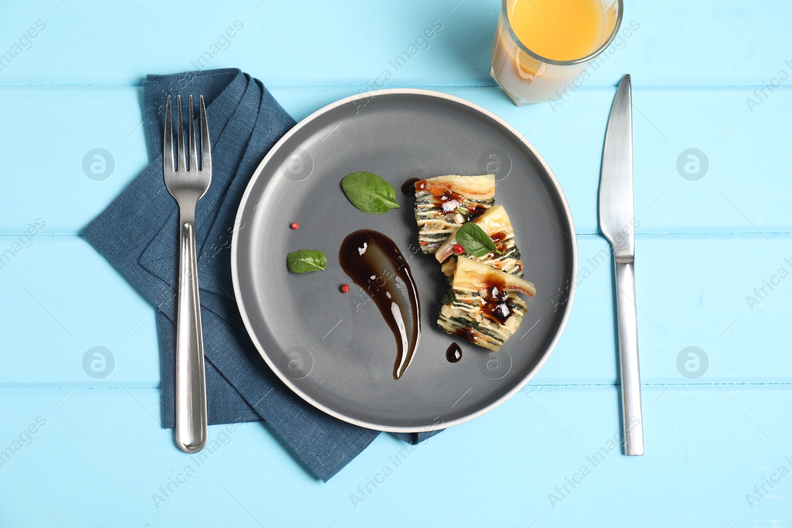 Photo of Pieces of tasty spinach lasagna served with orange juice on light blue wooden table, flat lay