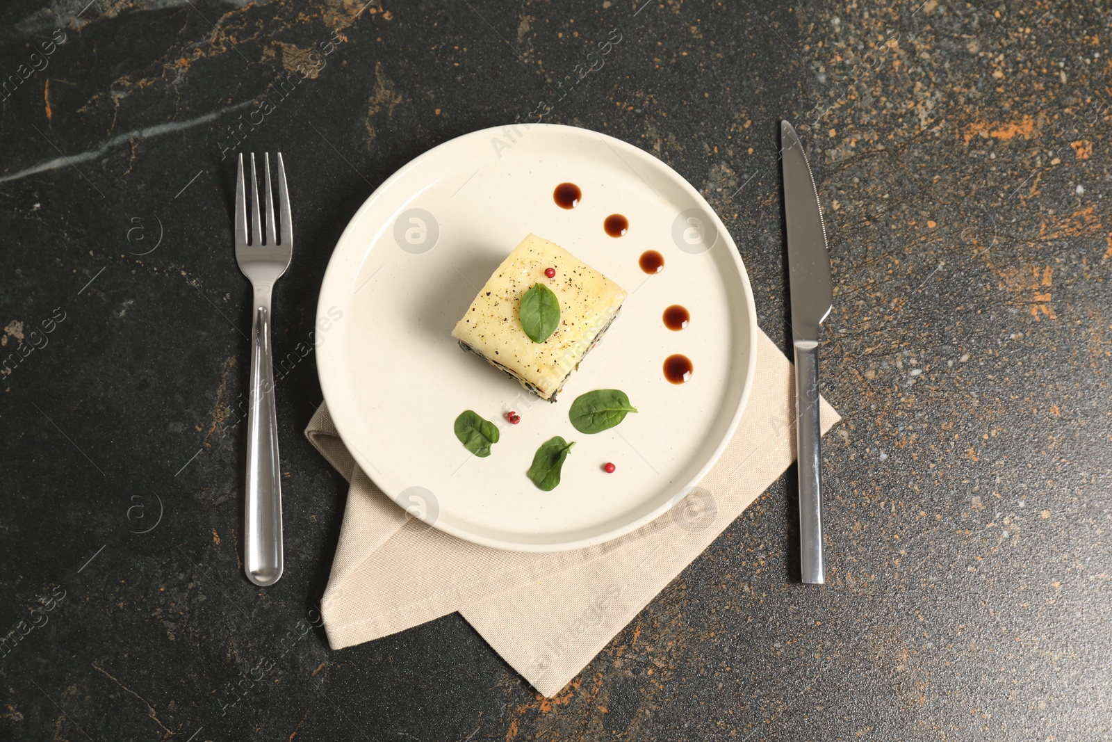 Photo of Piece of tasty spinach lasagna served on dark textured table, flat lay