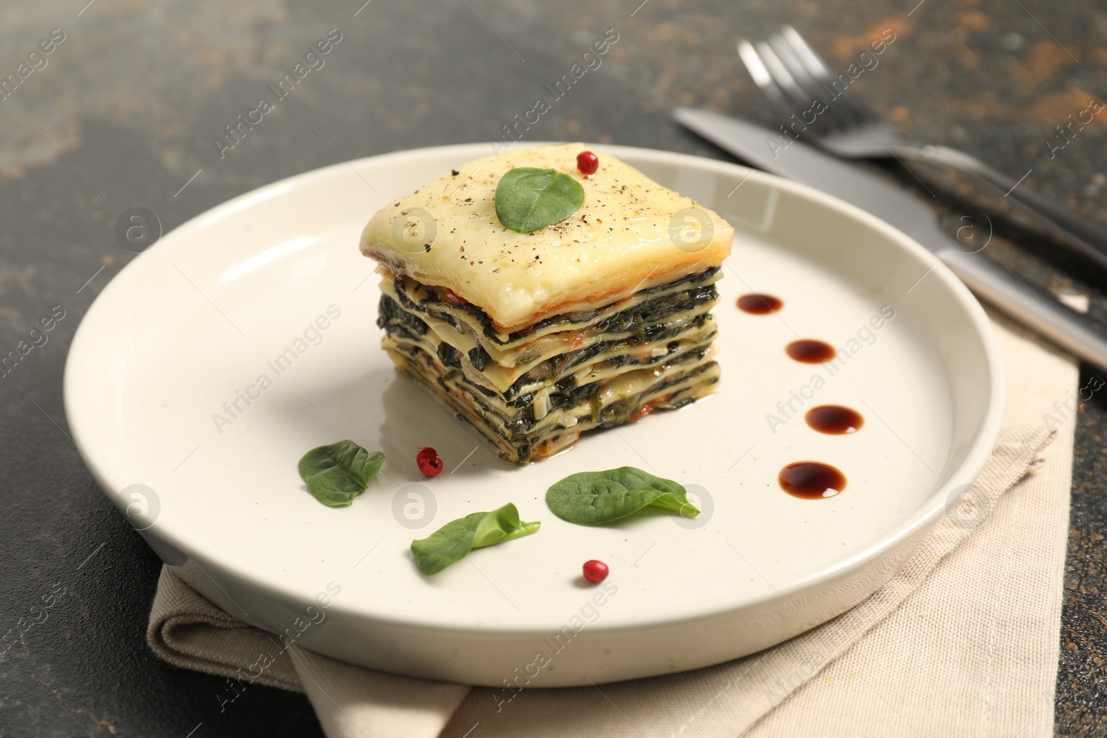 Photo of Piece of tasty spinach lasagna on dark textured table, closeup