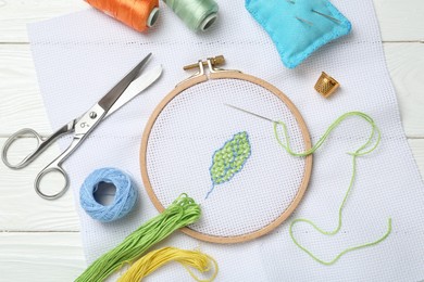 Photo of Embroidery and different sewing accessories on white wooden table, flat lay