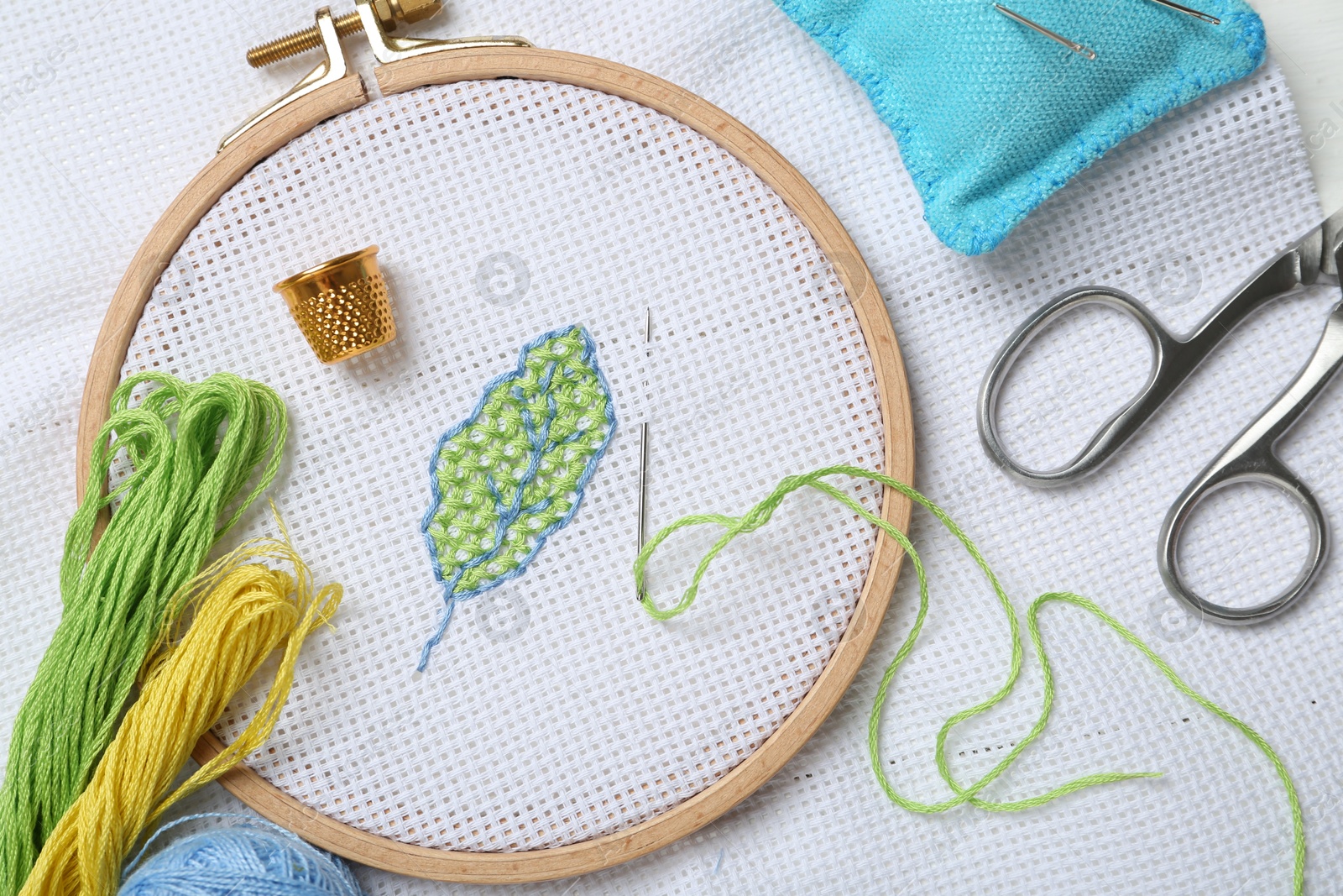 Photo of Embroidery and different sewing accessories on table, flat lay