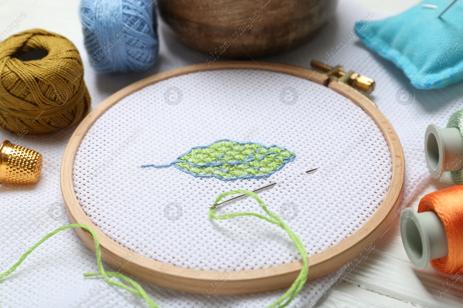 Photo of Embroidery and different sewing accessories on white wooden table, closeup