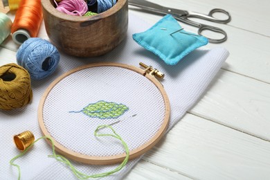 Photo of Embroidery and different sewing accessories on white wooden table, closeup