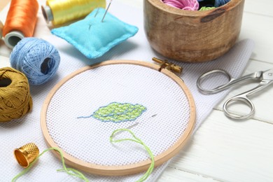 Photo of Embroidery and different sewing accessories on white wooden table, closeup