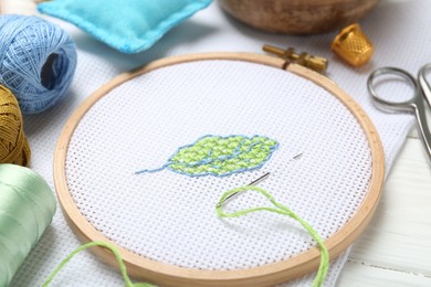 Photo of Embroidery and different sewing accessories on white wooden table, closeup