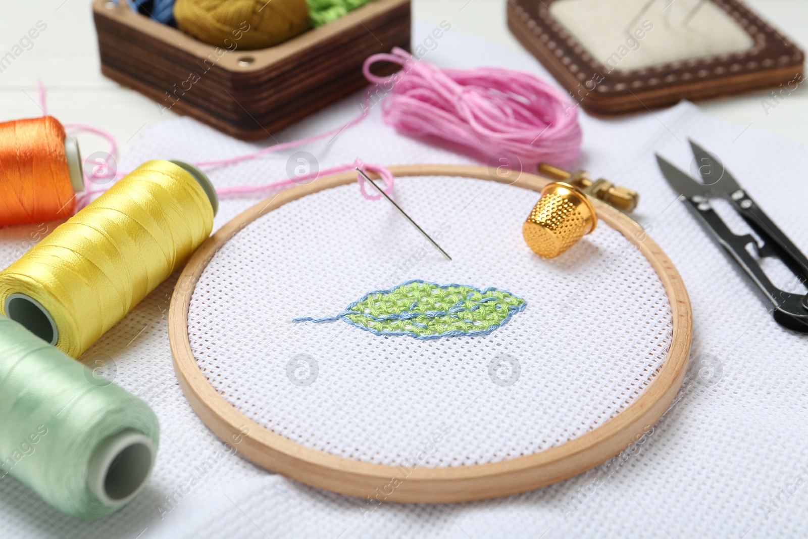 Photo of Embroidery and different sewing accessories on table, closeup