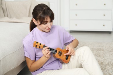 Photo of Woman playing ukulele on floor at home